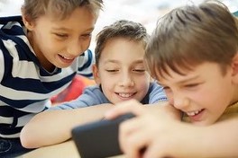 Elementary school age children all looking and smiling at a phone that one child is holding.